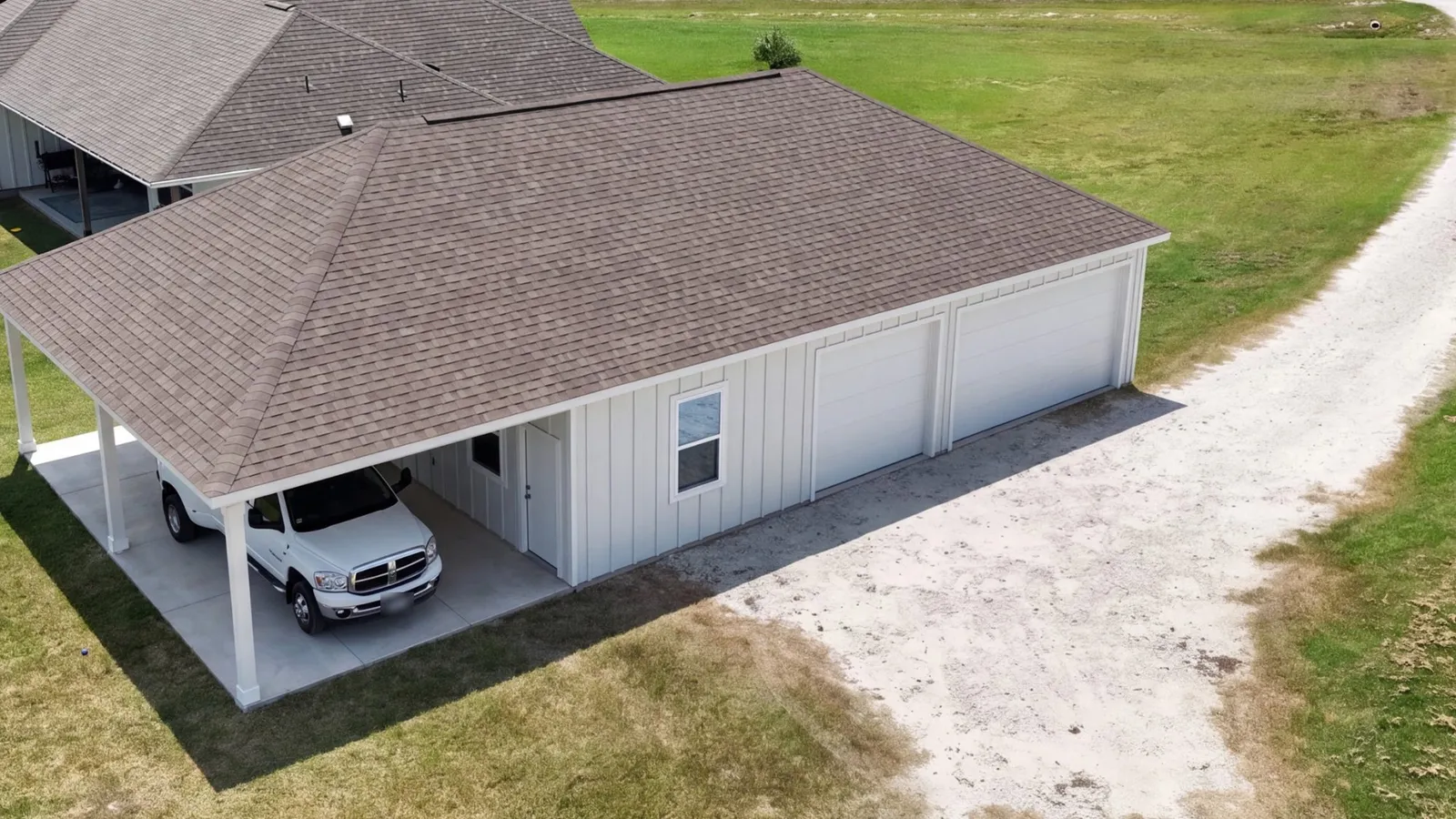 Concept render of a white garage with two overhead doors and a car port under a brown shingled hip roof, beside a gravel drive