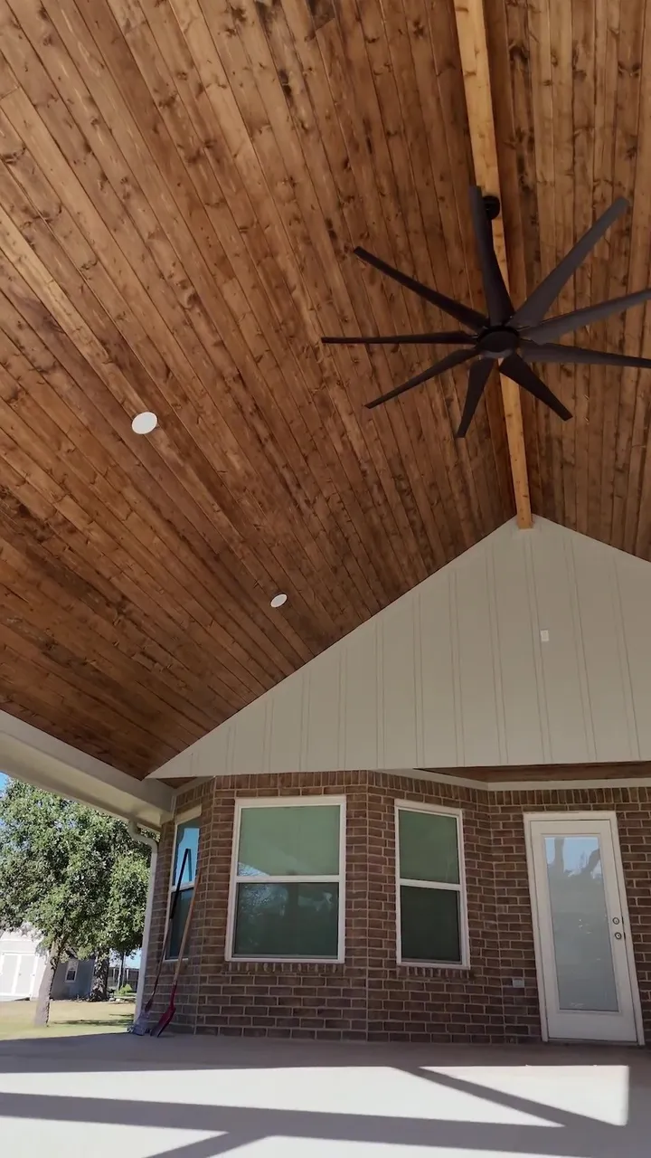 Stained cedar tongue and groove patio ceiling with a black ceiling fan