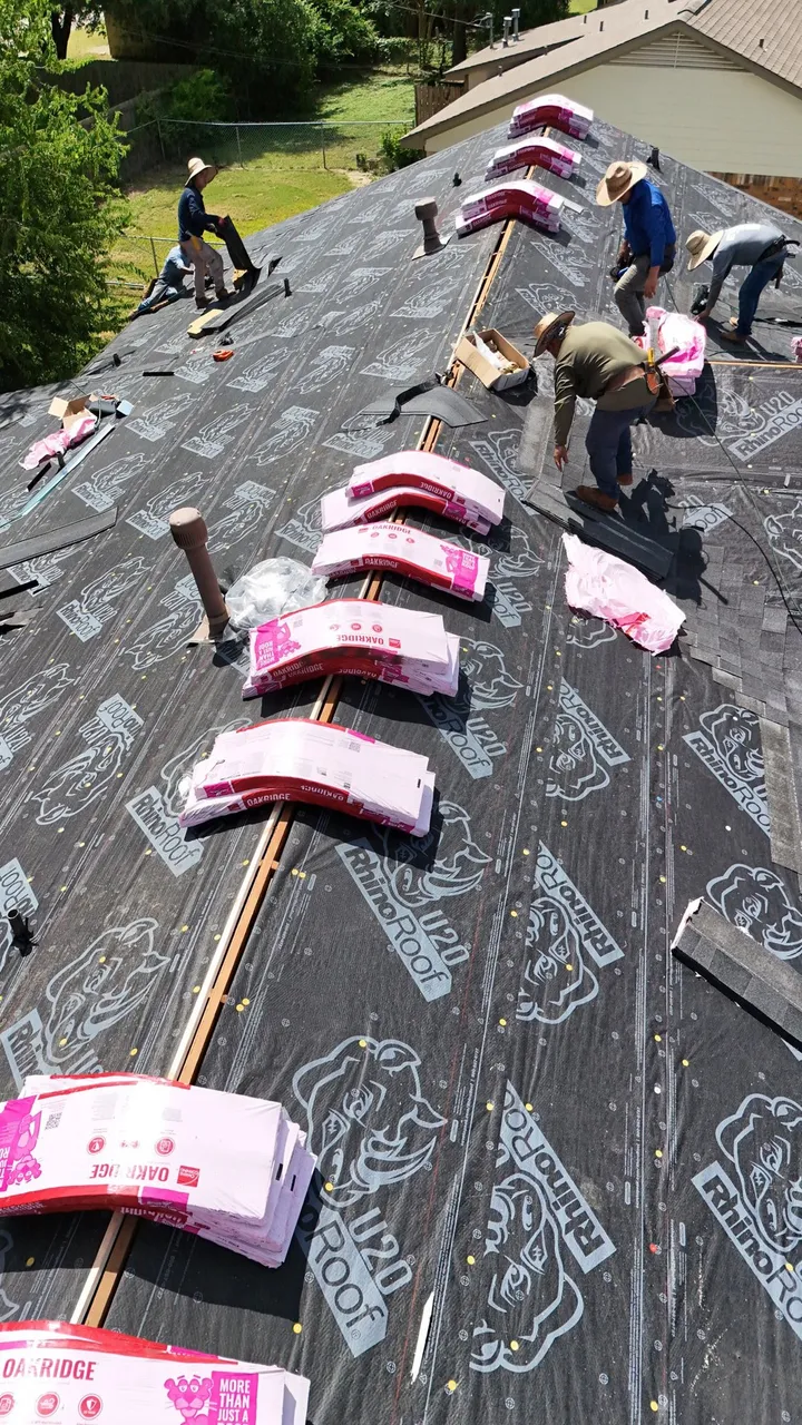 Roofers at work beside shingle bundles staged along the ridge